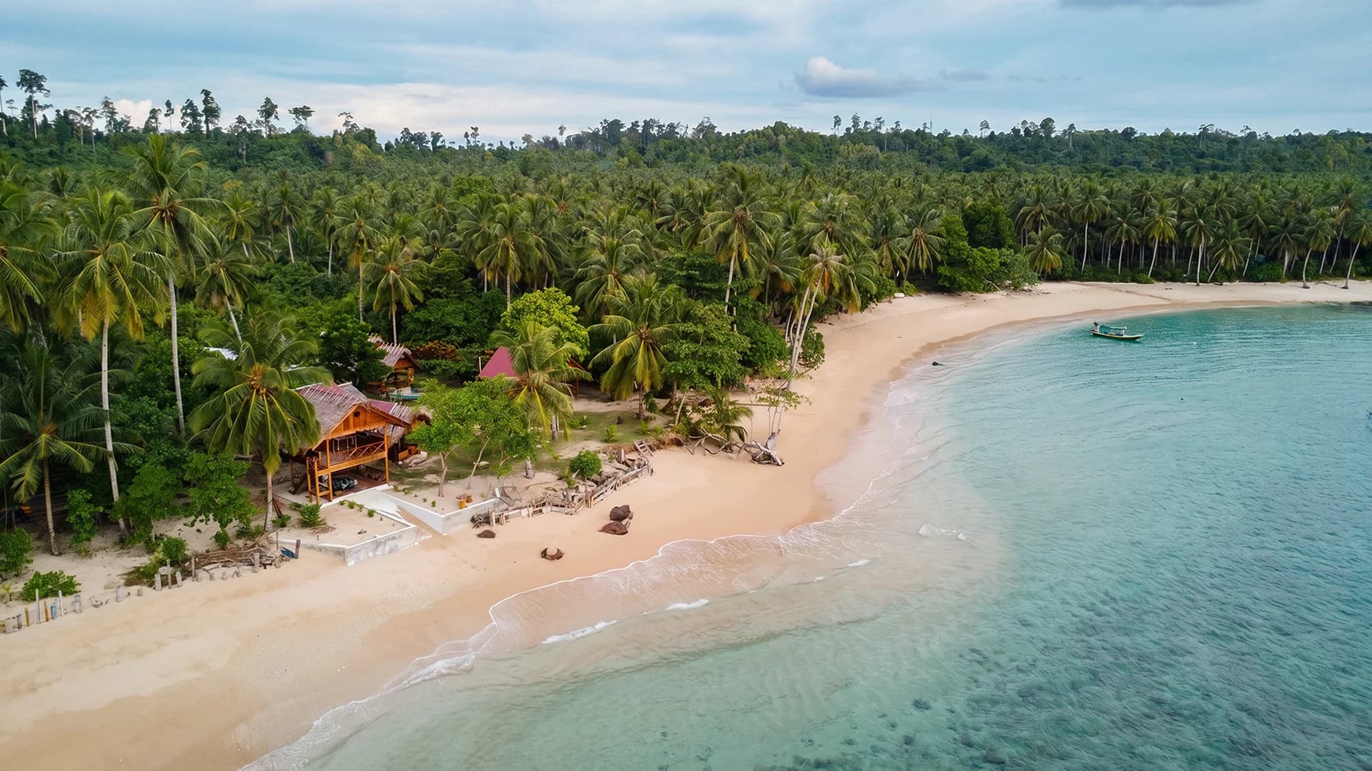 Aerial view of Purimanu’s beachfront camp, palm trees and sheltered bay